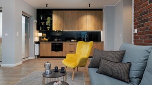 A modern living room with a sofa and a coffee table, a bright yellow chair, and a kitchen with wooden cabinets and a black countertop.