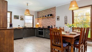 A modern kitchen with grey cabinets, a brick accent wall, and wooden dining chairs.