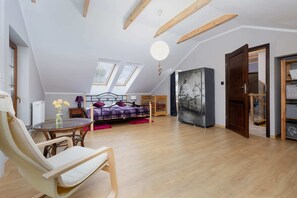 A spacious room with a high ceiling, wooden beams, a bed, a dining table with chairs, a small table with flowers, and a large painting on the wall.