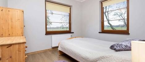 A bedroom with a bed, a wooden wardrobe, two windows with blinds, a radiator, and a purple rug.