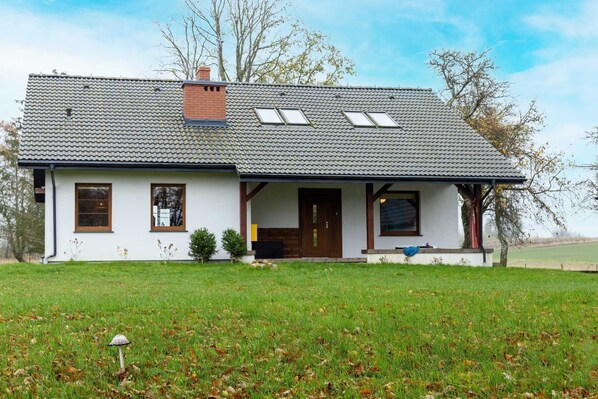 A two-story house with a sloped roof, a front porch, and a small garden area.