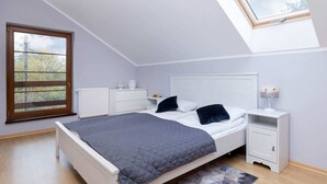 A bedroom with a skylight, a bed, a bedside table, a nightstand, and a radiator.