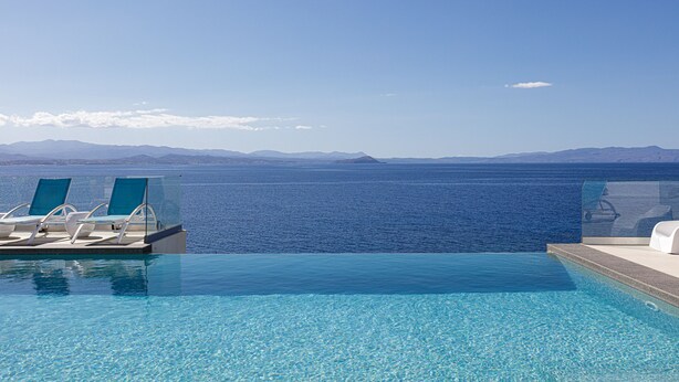 An infinity pool with clear blue water, lounge chairs, and a view of the sea and distant mountains. - Villa Chryssi - Hilltop Escape w/ Endless Sea Views by etouri (Chania)