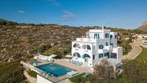 A white villa with a pool and multiple lounge chairs. - Villa Chryssi - Hilltop Escape w/ Endless Sea Views by etouri (Chania)