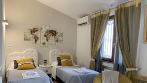 Ein Hotelzimmer mit zwei Betten, einem Sessel, einem kleinen Tisch und einem fenster mit Vorhängen.