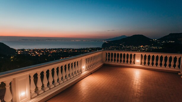 Ein Balkon mit Blick auf das Meer und die Stadtlichter im Dämmerlicht.