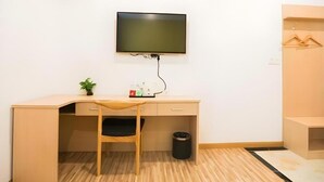 Een kamer met een bureau, stoel, televisie en een kleine plant.