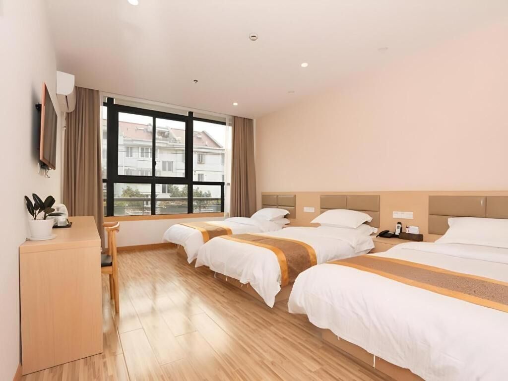 A hotel room with three beds, a desk, and a large window offering a city view.