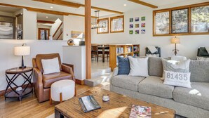 A spacious living room with a leather armchair, a grey sofa, and a wooden coffee table. A bookshelf filled with books is visible in the background. - Luxurious Ski-In/Ski-Out Telluride Mountain Escape (Mountain Village)