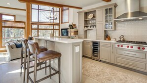 A modern kitchen with a central island, bar stools, a built-in stove, and a large window providing natural light. - Luxurious Ski-In/Ski-Out Telluride Mountain Escape (Mountain Village)
