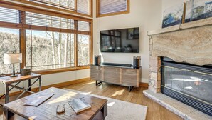 A living room with large windows, a fireplace, a television, and a wooden coffee table. - Luxurious Ski-In/Ski-Out Telluride Mountain Escape (Mountain Village)