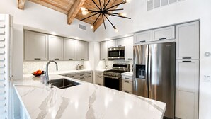 Uma cozinha moderna com bancada de mármore, eletrodomésticos de aço inoxidável e uma luminária de teto diferenciada.