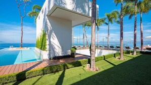 Ein modernes Haus mit Pool, umgeben von Palmen und freiem Blick auf den Ozean.