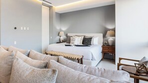 A modern hotel room with a bed, bedside tables, a sofa, and a small table.