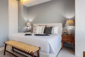 Une chambre à coucher bien rangée, avec un lit, des tables de chevet, un banc et des lampes fixées au mur.