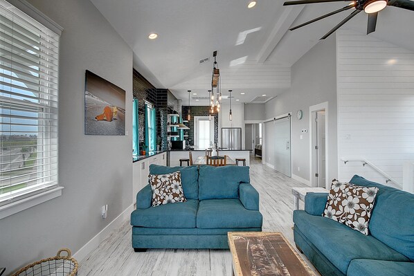 A modern living room with teal sofas, a wooden coffee table, and a kitchen in the background.