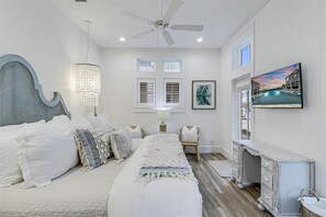 Une chambre à coucher comprenant un lit, un lustre, un ventilateur de plafond, une télévision, une commode et une fenêtre avec des volets.