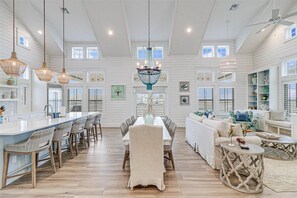 Une cuisine spacieuse dotée d’un îlot central, un coin repas agrémenté d’un lustre, et un salon avec un canapé et une table basse.