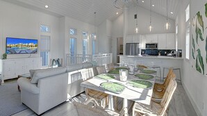 Un salón espacioso con un televisor grande, una mesa de comedor con sillas y una cocina al fondo.