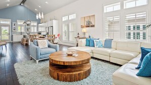Amplio salón con una gran mesa redonda de madera, un sofá color beige y un sillón azul.