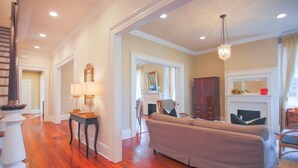 A spacious living room with hardwood flooring, a white sofa, a fireplace, and a chandelier. - Gorgeous Estate Near Forsyth w/ Parking, Courtyard by Lucky Savannah (Savannah)