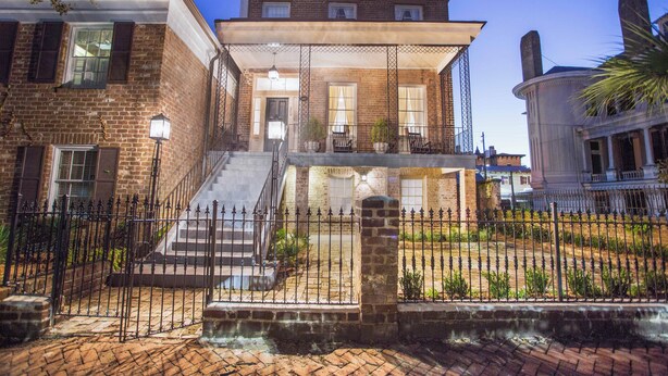 A historic brick building with a covered porch, a staircase, and a fenced courtyard. - Gorgeous Estate Near Forsyth w/ Parking, Courtyard by Lucky Savannah (Savannah)