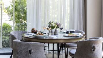 Un comedor con una mesa redonda, sillas tapizadas en gris y vistas a zonas verdes a través de cortinas traslúcidas.