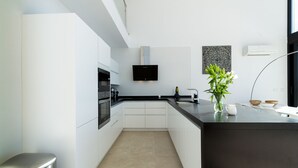 Une cuisine moderne avec des meubles blancs, un plan de travail noir, un four encastré, un téléviseur fixé au mur et une petite plante posée sur le plan de travail.
