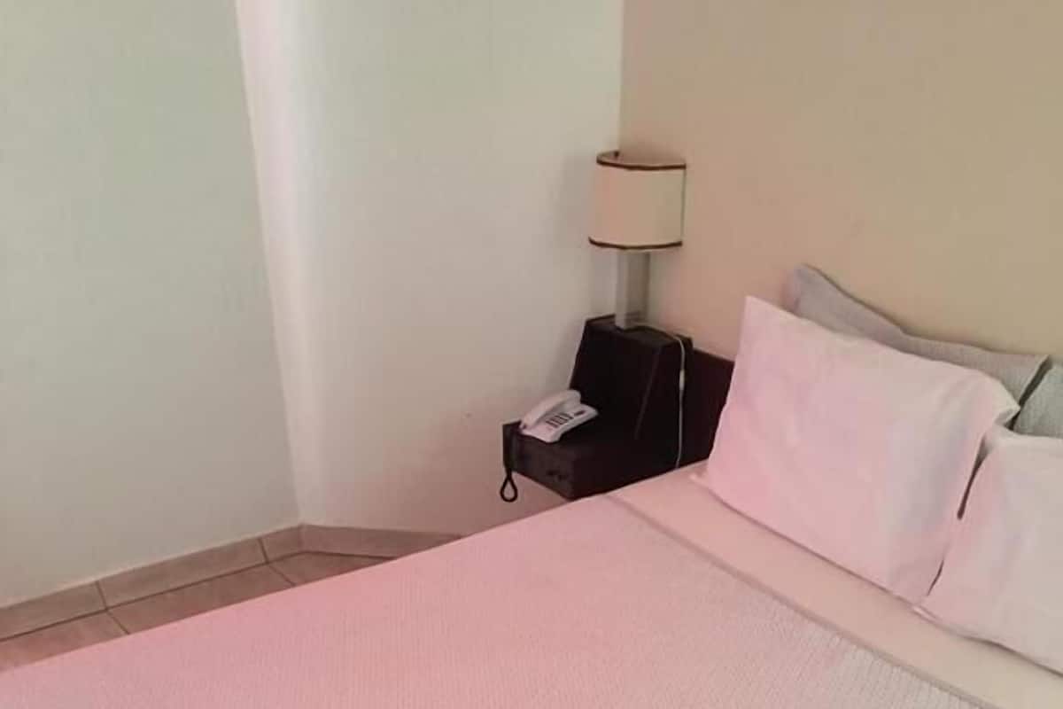Una cama bien tendida con una colcha rosa y dos toallas blancas dobladas.