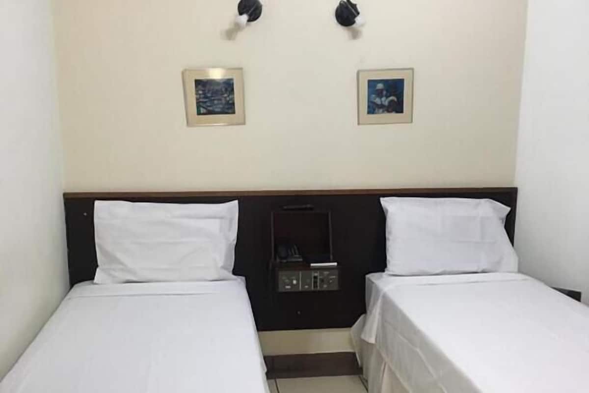 Una habitación sencilla y limpia con dos camas individuales, una mesita de noche pequeña y dos lámparas de pared.
