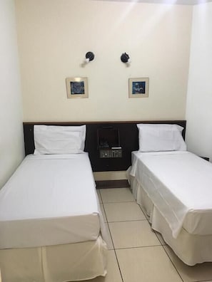 A simple, clean room with two single beds, a small bedside table, and two wall-mounted lamps.