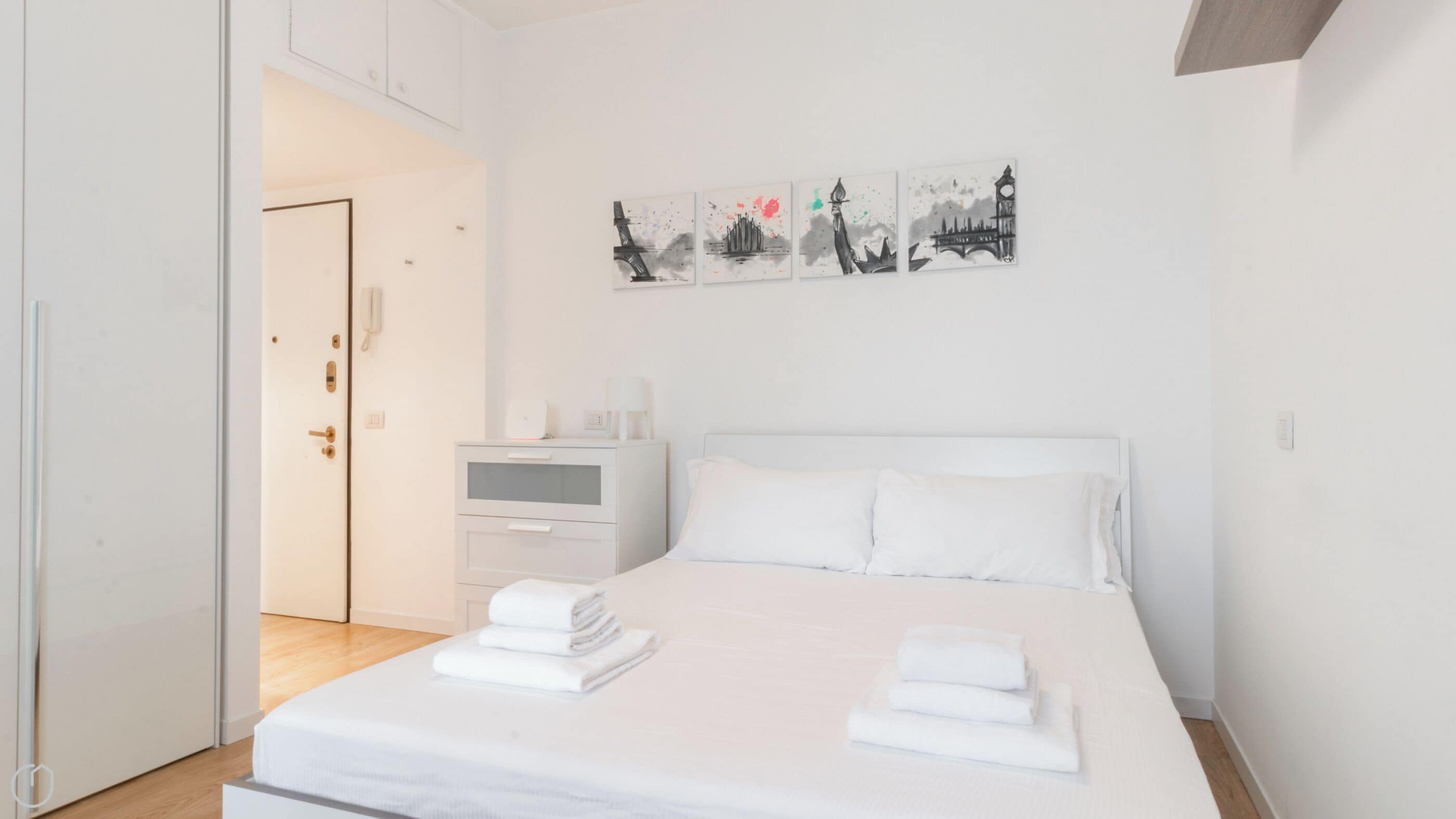A hotel room with a bed, a bedside table, a nightstand, and a wall-mounted artwork.