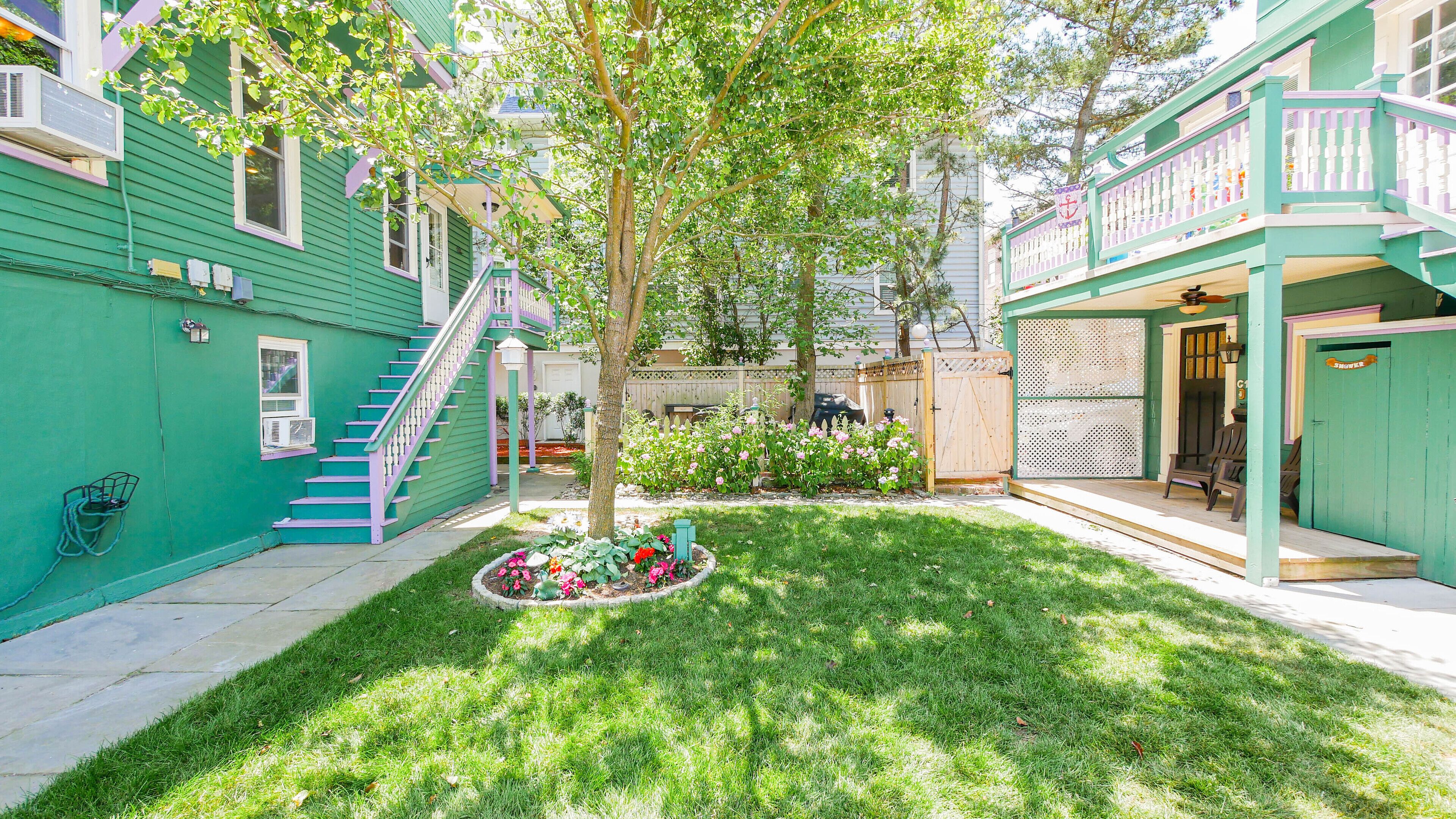 A green building with a staircase, a tree, and a flower bed.