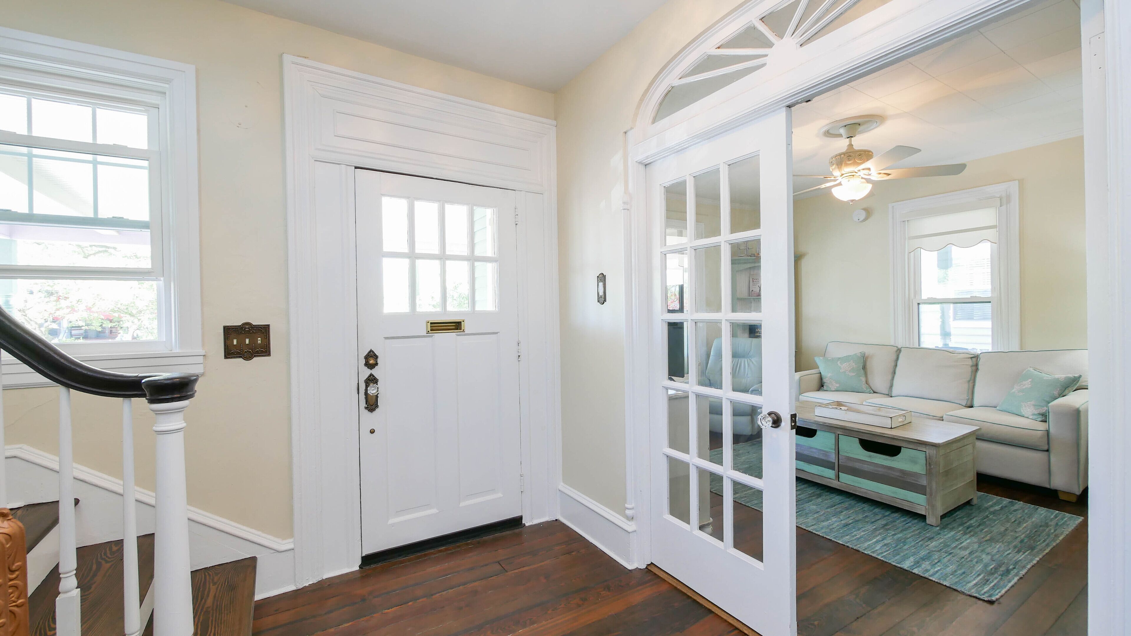 A hallway with a white door, a staircase, and a living room with a sofa and a coffee table.