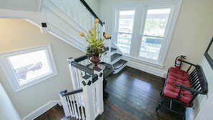 A staircase with a white railing, a red cushioned chair, and a vase with flowers on the landing. - One of a kind single family home, 6 bedrooms, sleeps 13 (Ocean City)