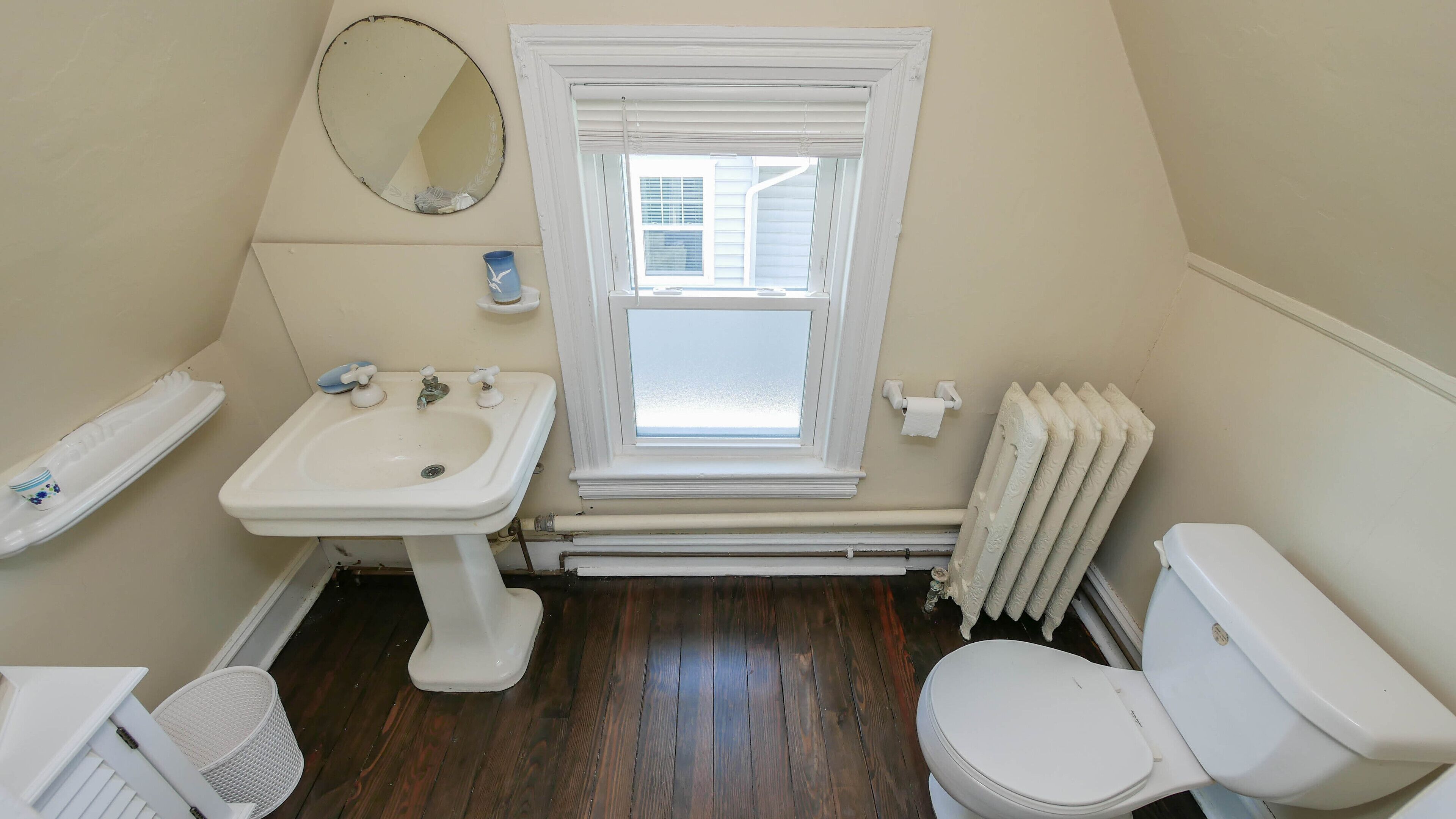 Un baño pequeño y limpio con lavamanos, inodoro y ventana blancos.