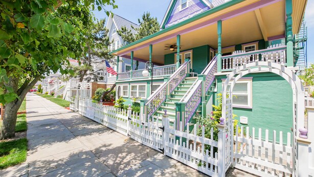 A two-story house with a white picket fence, a porch, and a staircase leading to the second floor. - One of a kind single family home, 6 bedrooms, sleeps 13 (Ocean City)