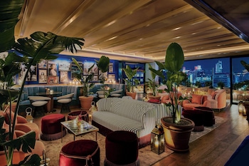 A rooftop bar with a view of a cityscape and mountains, featuring tables, chairs, and a decorative fountain. at The Hollywood Grande, Autograph Collection