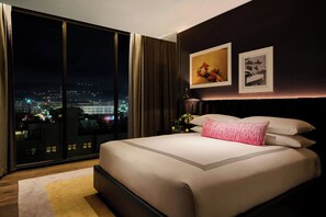 A modern hotel room with a large bed, a night view of a cityscape, and two framed pictures on the wall.