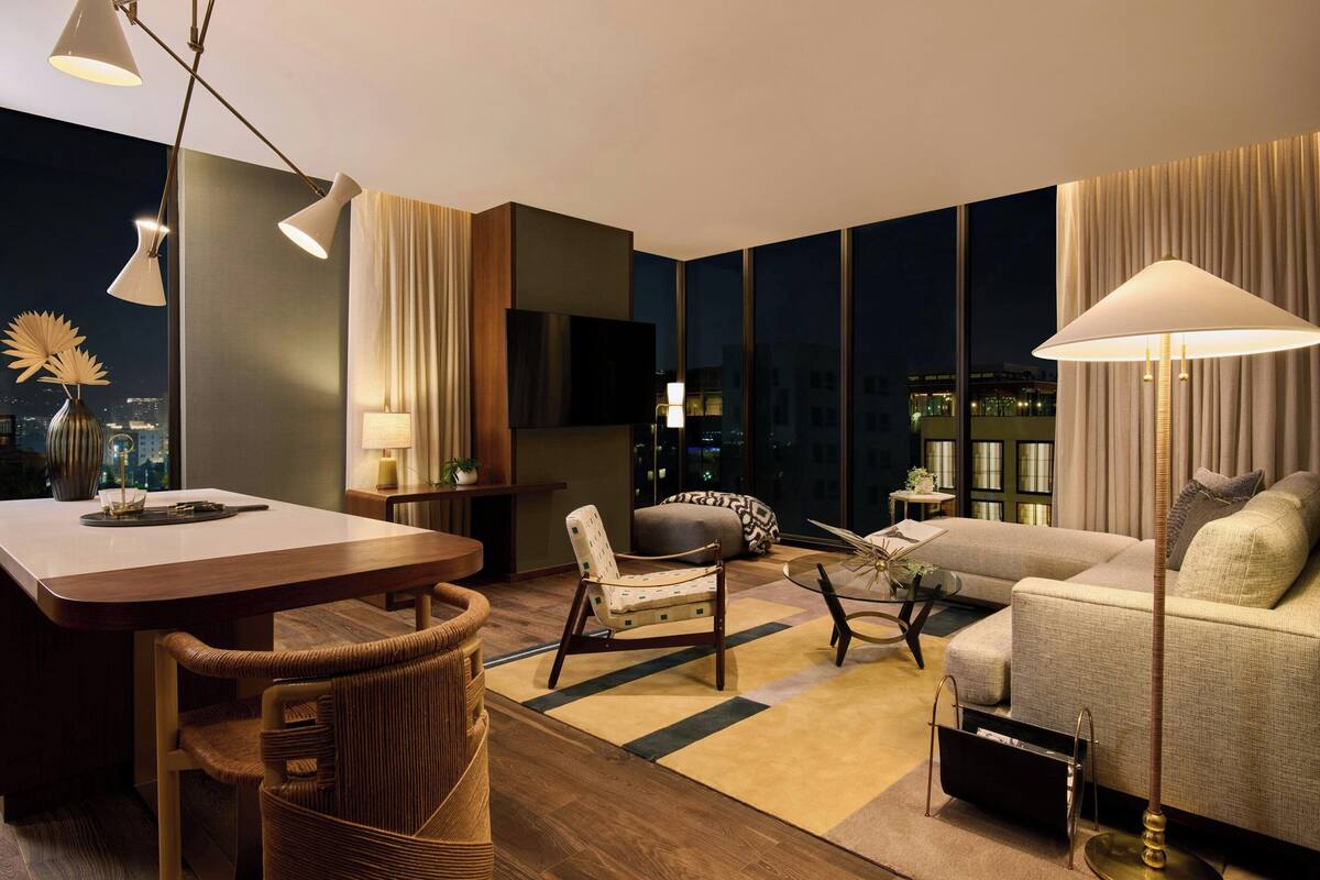 A modern living room with a sofa, armchair, dining table, and a large window offering a city view.