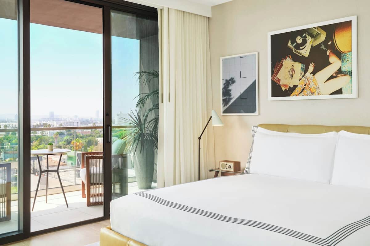A hotel room with a large bed, a balcony with a table and chairs, and a city view.