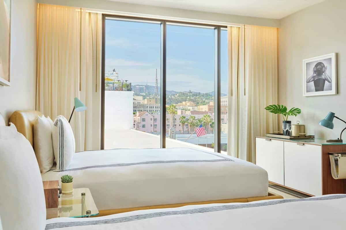A hotel room with a large bed, a desk with a lamp, a view of the city, and a plant on the desk.