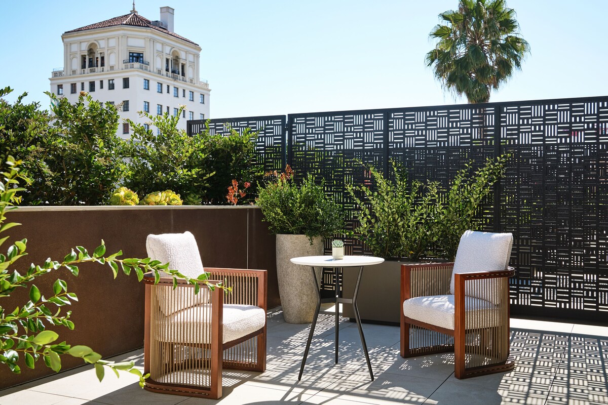 A balcony with two wicker chairs, a small round table, and a decorative black fence.