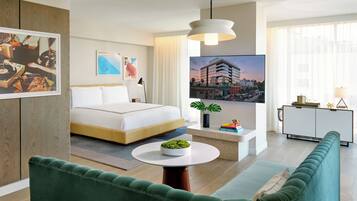 A modern hotel room with a bed, a round table with a plant, a green sofa, and a cityscape view.