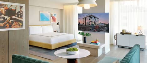 Une chambre d’hôtel moderne avec un lit, une table ronde agrémentée d’une plante, un canapé vert et une vue sur le paysage urbain.