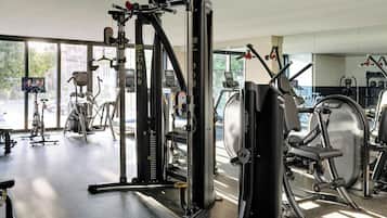Un gimnasio con diversas máquinas de ejercicio, amplias ventanas y vistas a la calle.