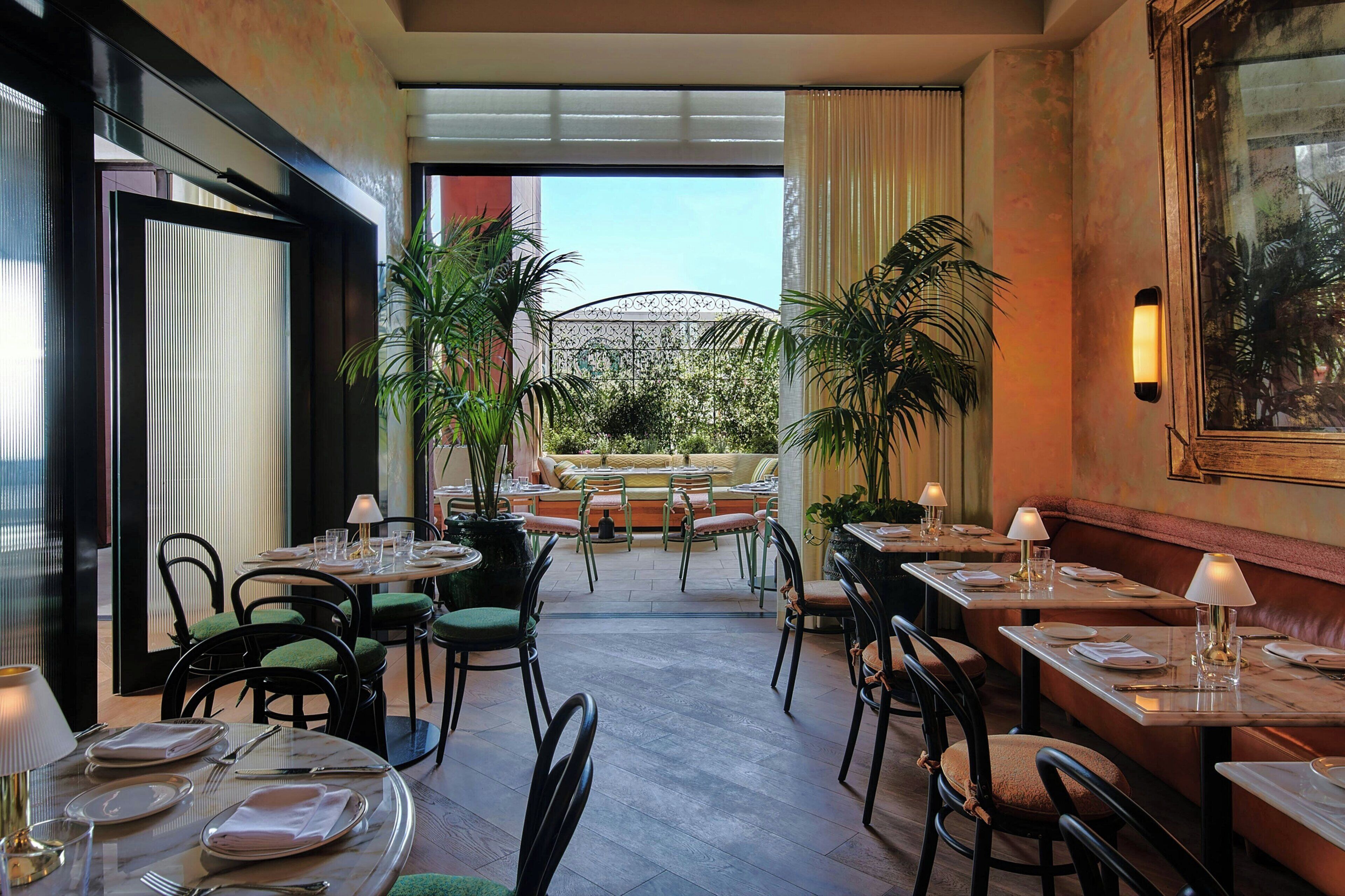 Un restaurante con mesas y sillas, vistas al exterior y plantas en macetas.