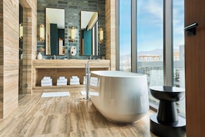 A modern bathroom with a large bathtub, a vanity with a mirror, and a view of a cityscape through large windows.