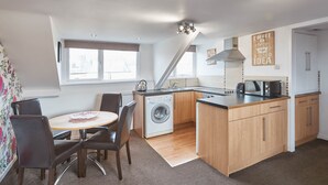 A compact kitchen with a washing machine, a microwave, and a dining area with a table and chairs. - Apartment 4 At Glencoe (Whitby)