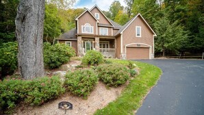 A two-story house with a front porch, stone foundation, and a garage. - Cozy Family Mountain Home in Seven Springs (CHAMPION)
